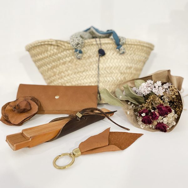 Cesta regalo que incluye: un cesto de mimbre, un ramito de flores, un abanico de manera, un llavero de piel, una funda de gafas de piel y un imperdible, todo artesanal hecho a mano.